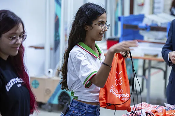 Uma aluna recebe uma mochila do Instituto Panapaná durante um encontro do Alagoas Tech, em Maceió (AL), 2025